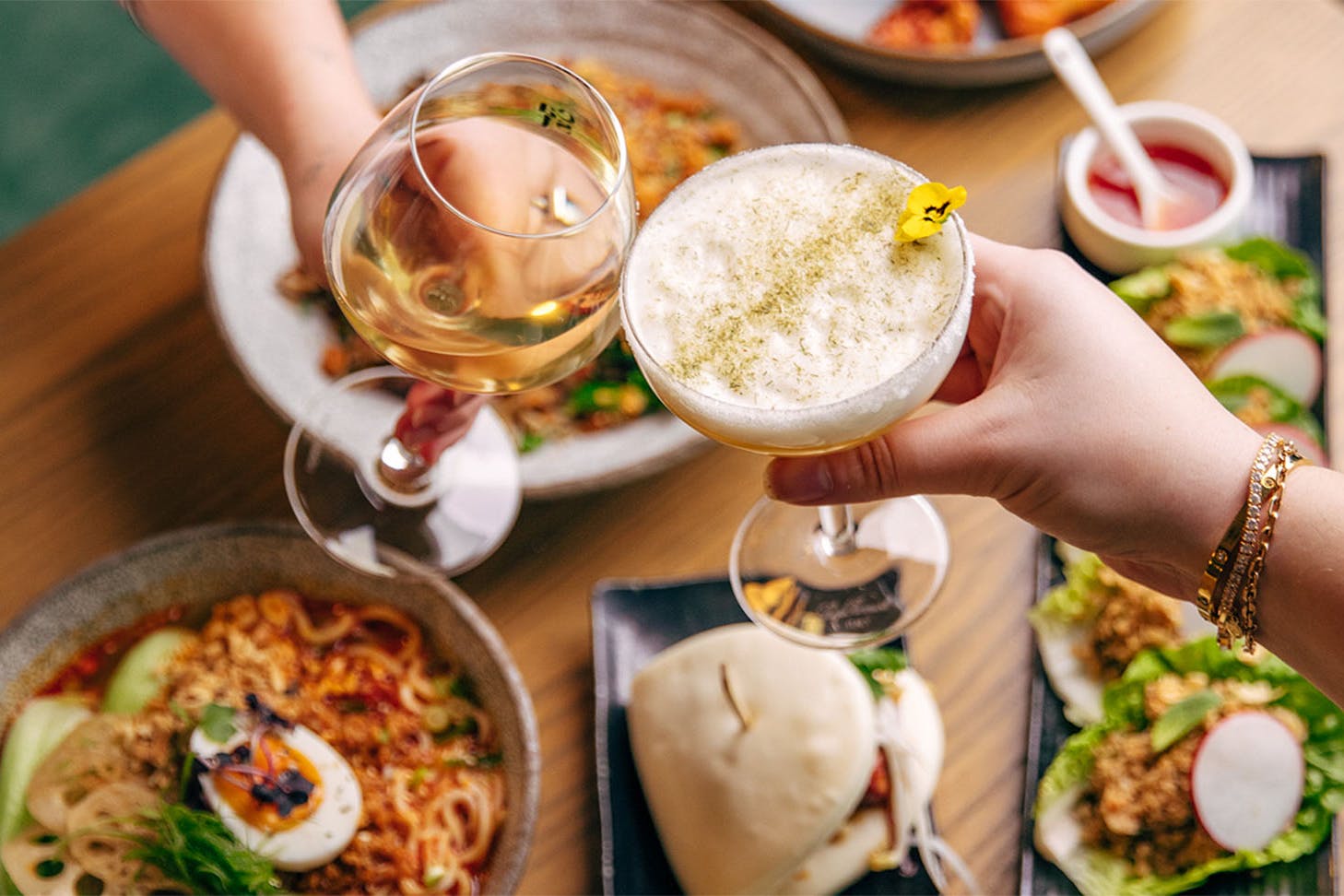 Two people cheers over a fine spread of vegetarian food.
